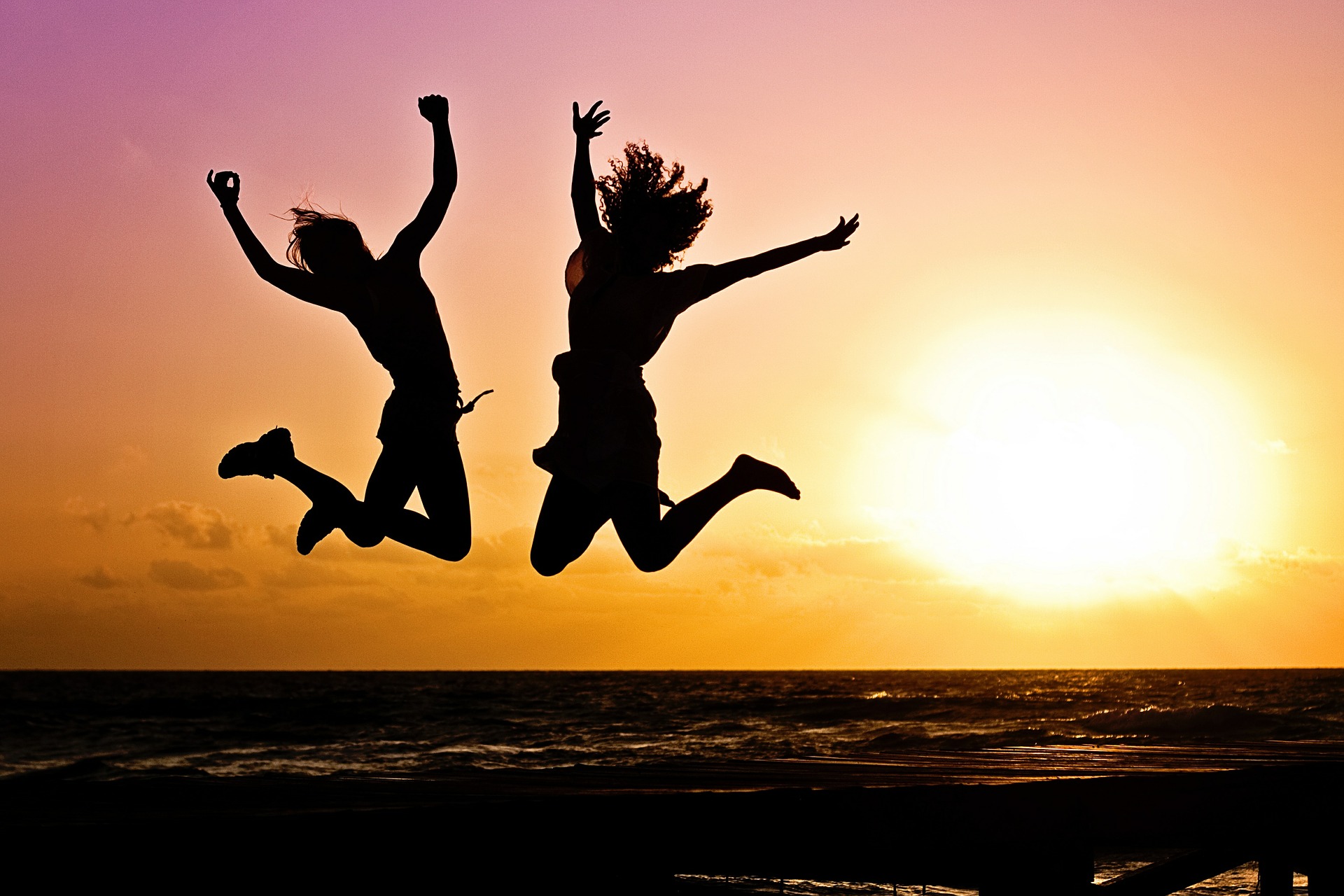 Image: two silhouettes jumping in the air with sunset background
